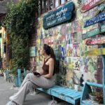 Jeune femme assise sur un banc bleu devant un mur coloré dans la vieille ville de Tbilissi, Géorgie